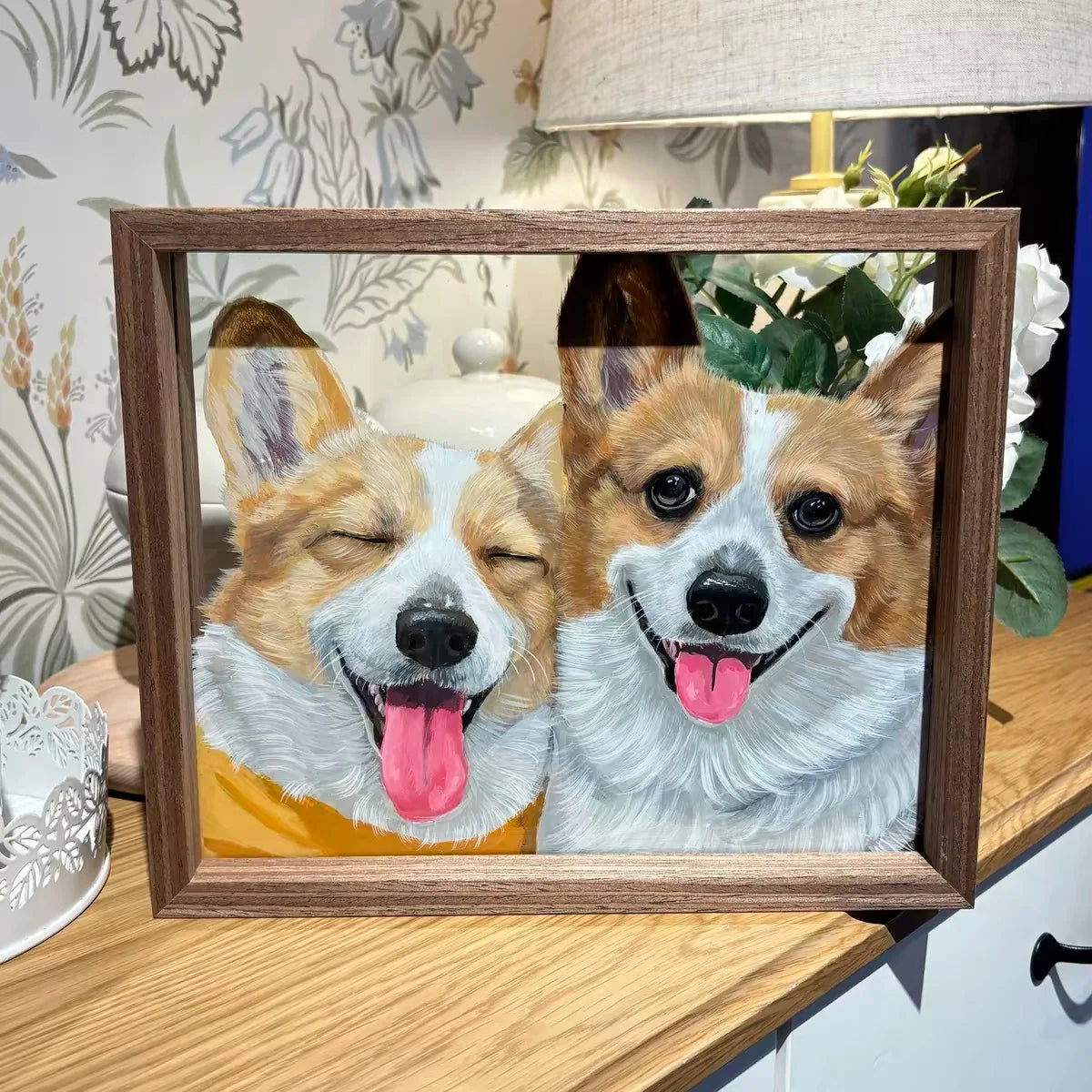 Two-corgi frame on wooden table with lamp and plant.
