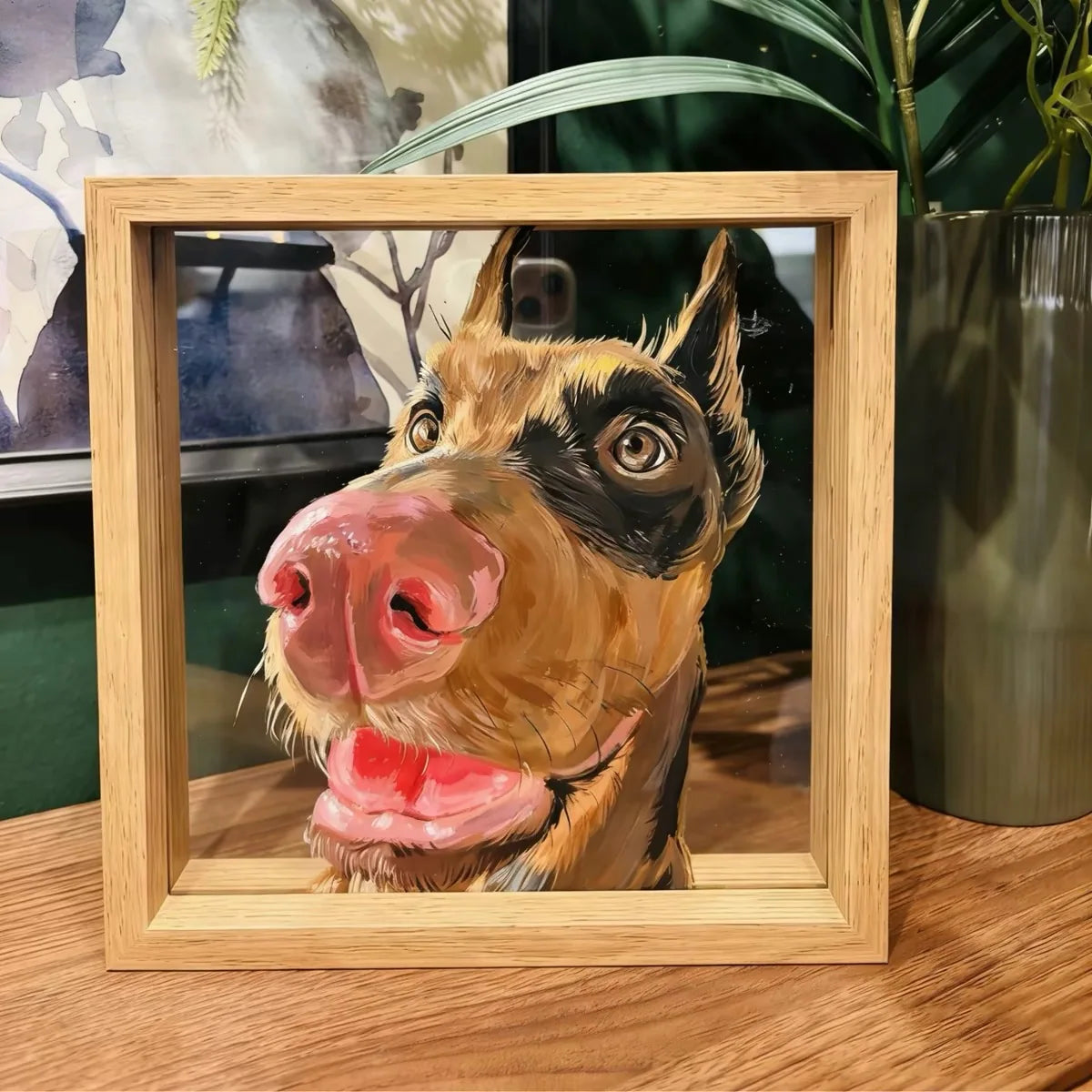 Doberman portrait frame on wooden desk with plants behind.