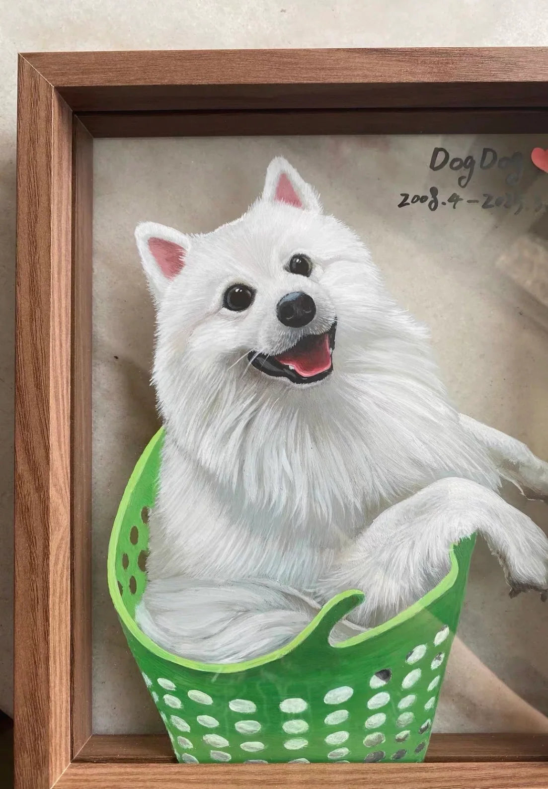 Close view of white dog sitting in green basket painted in wood frame.