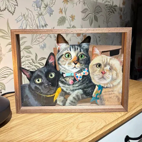 Three-cat frame on wooden table with lamp and botanical wallpaper.