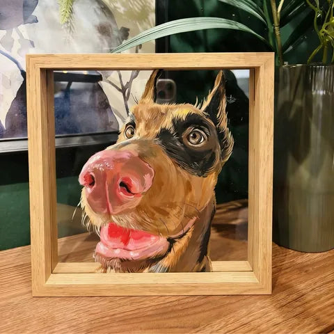 Doberman portrait frame on wooden desk with plants behind.